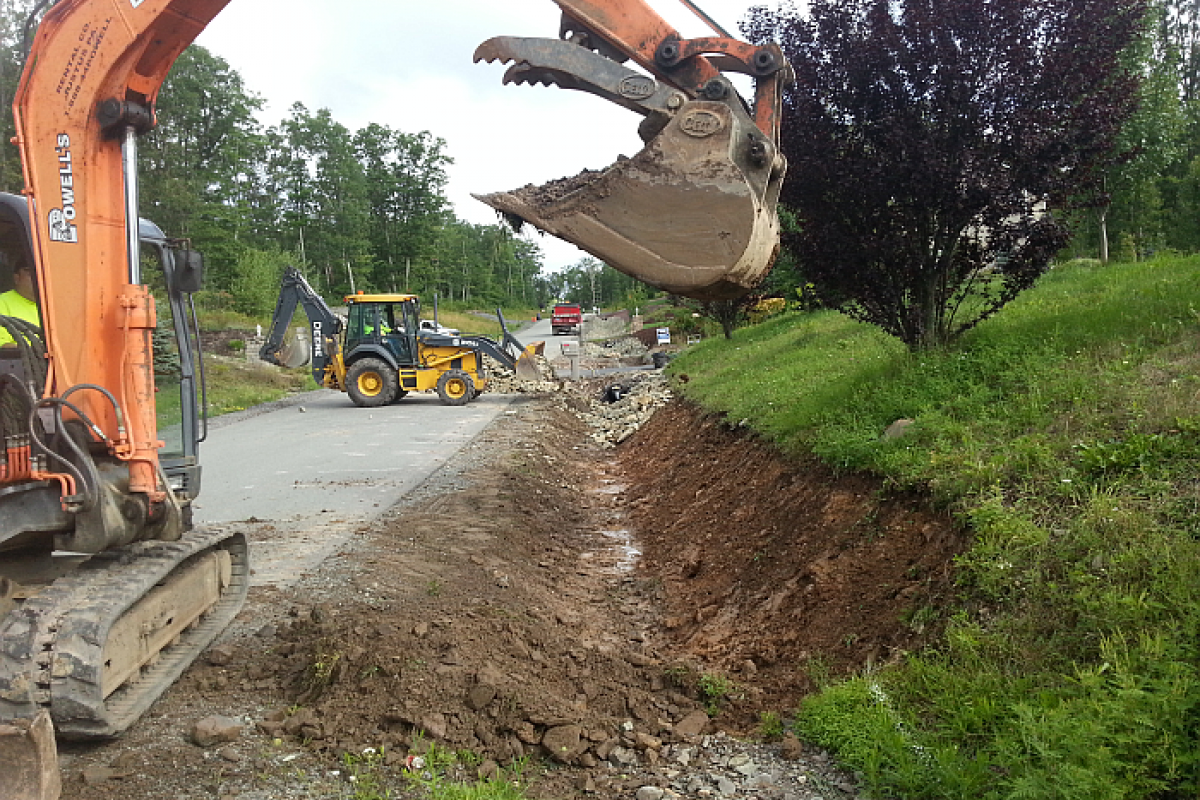 Ditch repair along Windsor Way: bucket of front loader posed over large trench running parallel to road
